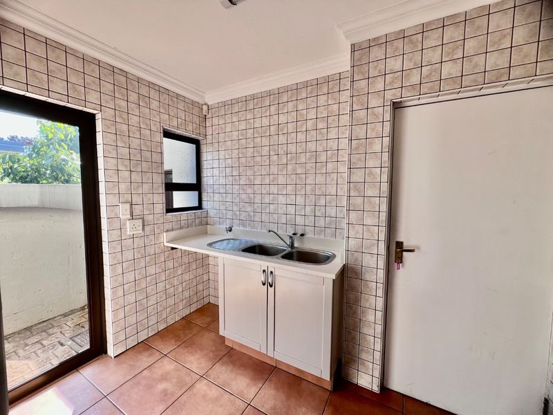 A functional laundry area featuring tiled walls and flooring, a double basin stainless steel sink with built-in cabinetry, and direct access to an outdoor space.