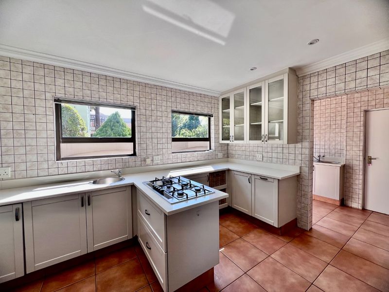 A functional kitchen featuring light-toned cabinetry, a gas cooktop, tiled splashbacks, and direct access to a separate scullery area.