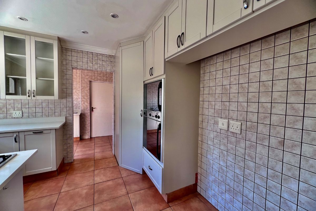 A functional kitchen featuring built-in cabinetry, a wall-mounted oven, and tiled finishes throughout, offering a clean and neutral space ready for updates.