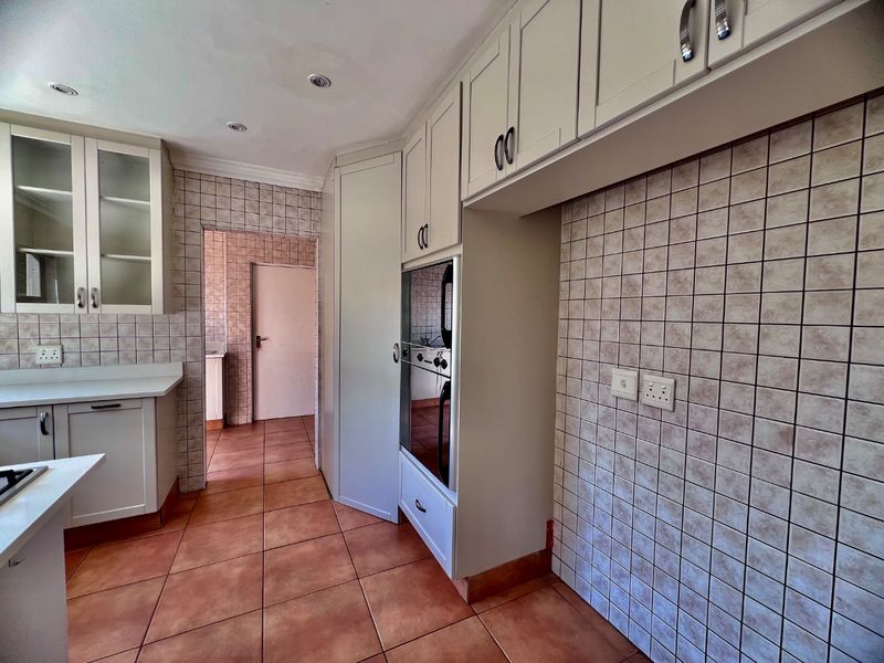 A functional kitchen featuring built-in cabinetry, a wall-mounted oven, and tiled finishes throughout, offering a clean and neutral space ready for updates.