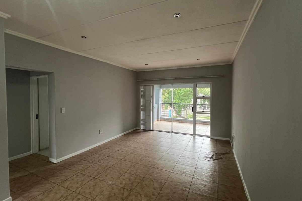 A spacious, empty living room featuring neutral grey walls, tiled flooring, recessed lighting, and a sliding glass door providing access to an outdoor balcony.