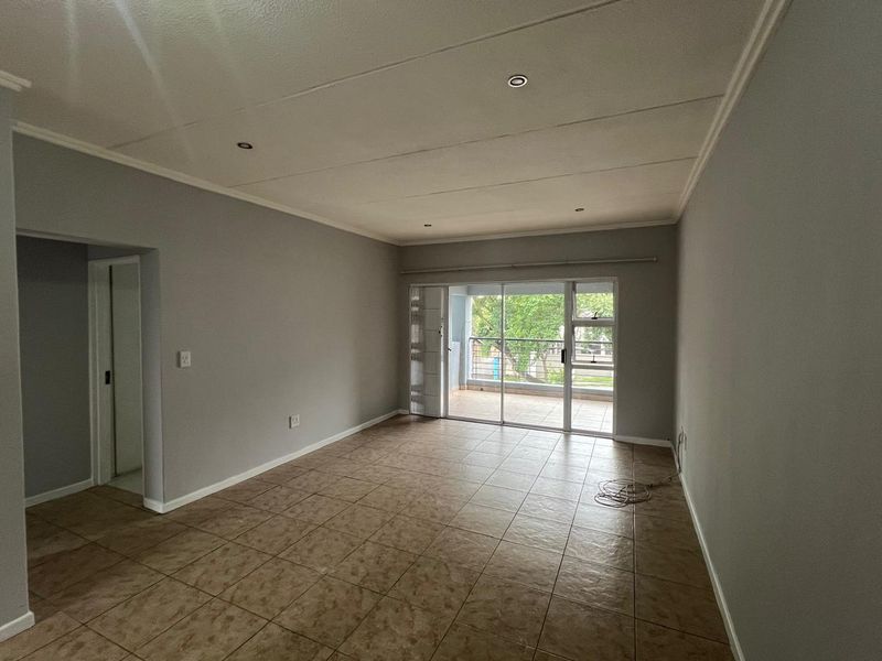 A spacious, empty living room featuring neutral grey walls, tiled flooring, recessed lighting, and a sliding glass door providing access to an outdoor balcony.