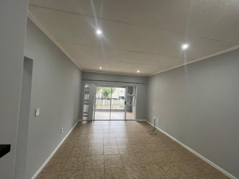 An empty, well-lit living room featuring neutral grey walls, tiled flooring, and a sliding glass door providing access to an outdoor area.