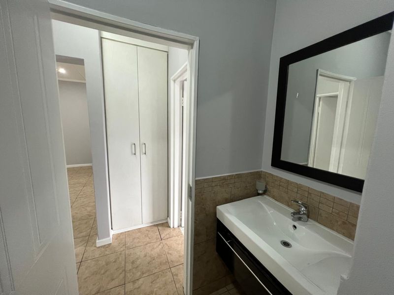 A clean bathroom featuring a modern vanity basin with mixer tap, tiled splashback, and built-in storage cupboard, with neutral tiled flooring throughout.