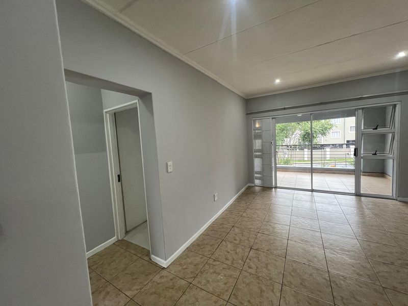 A bright, empty living area featuring neutral grey walls, tiled flooring, and a sliding glass door providing access to an outdoor balcony.