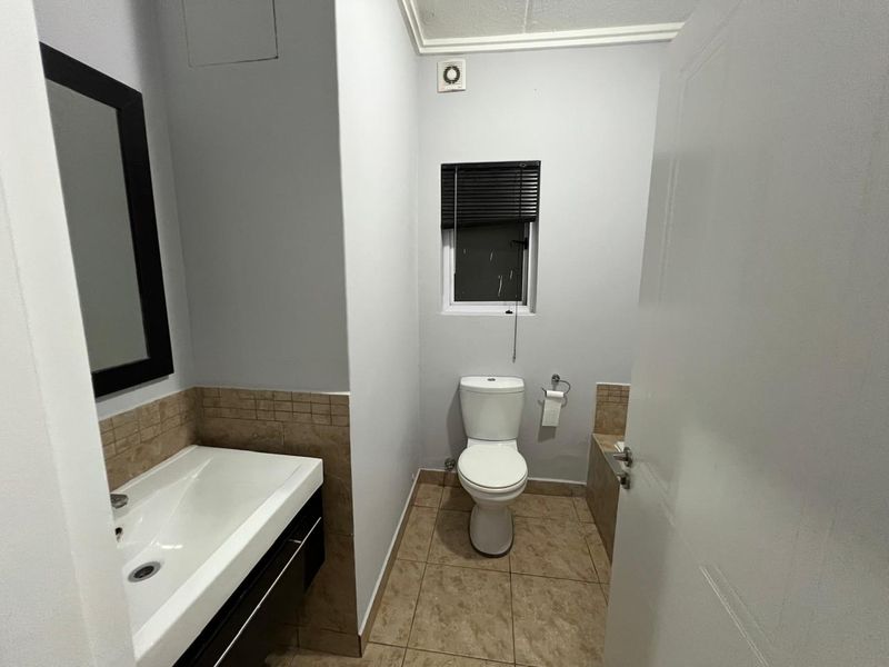 A clean and functional bathroom featuring a vanity basin, toilet, tiled flooring, and an extractor fan.