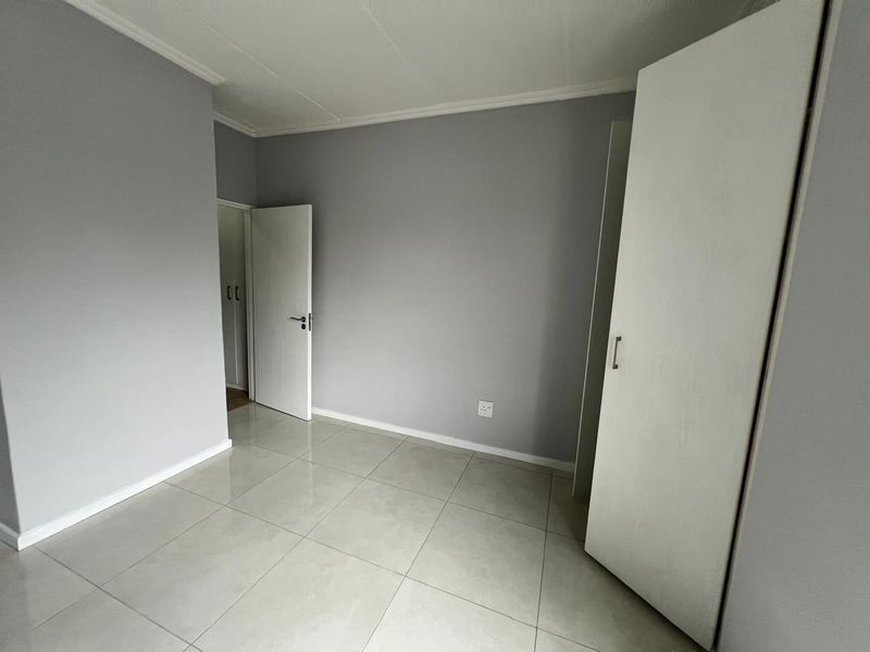 A clean, empty bedroom featuring neutral grey walls, large format floor tiles, and a built-in wardrobe.