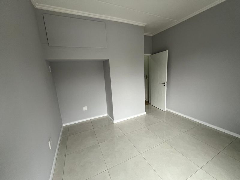 A clean, empty bedroom featuring neutral grey walls, tiled flooring, and white trim, providing a versatile space ready for personalization.