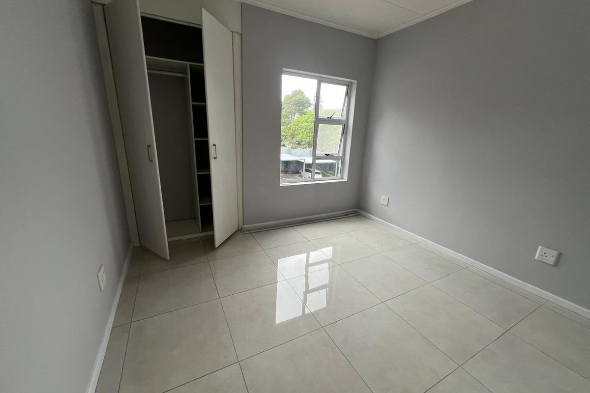 A bright, empty bedroom featuring neutral grey walls, polished light-colored floor tiles, and a built-in wardrobe with shelving.