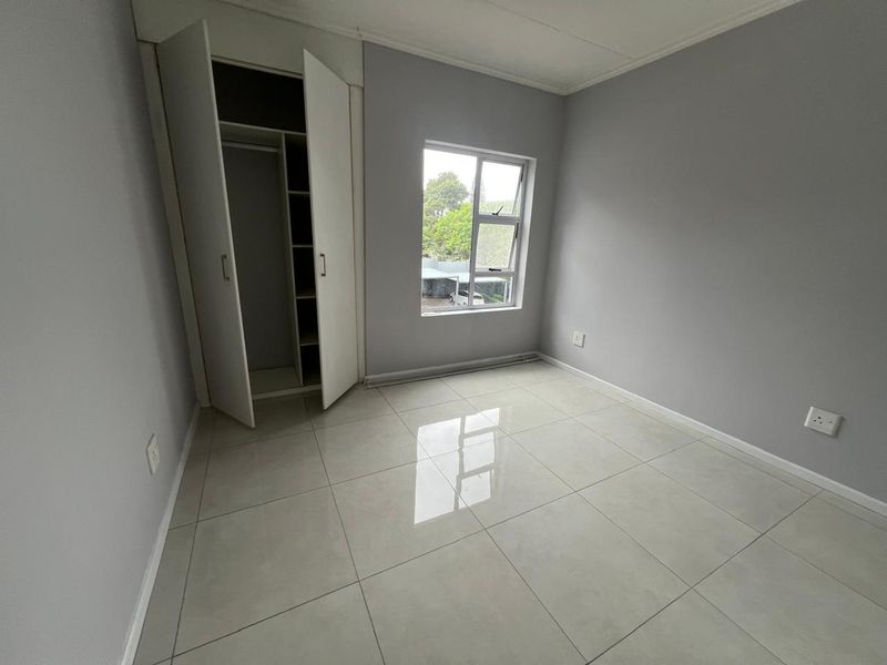A bright, empty bedroom featuring neutral grey walls, polished light-colored floor tiles, and a built-in wardrobe with shelving.