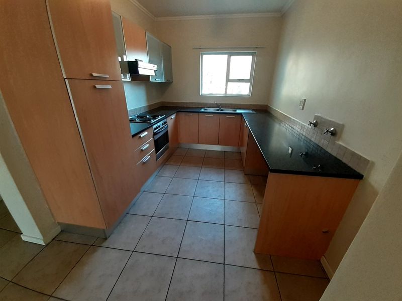 A functional kitchen featuring light wood-tone cabinetry, dark laminate countertops, built-in oven and hob, and tiled flooring in a clean, vacant space.