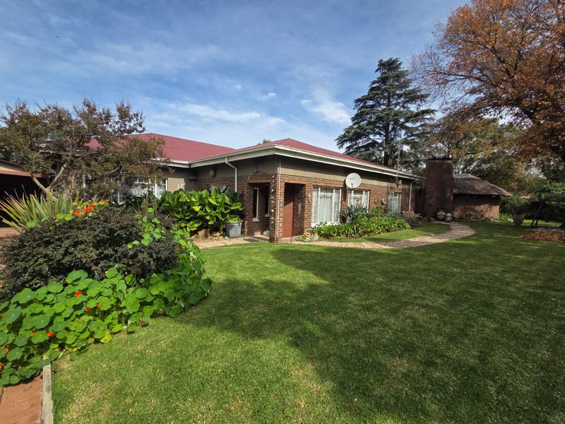 A well-maintained single-story brick house featuring a metal roof, established garden, and a paved walkway leading to the entrance.