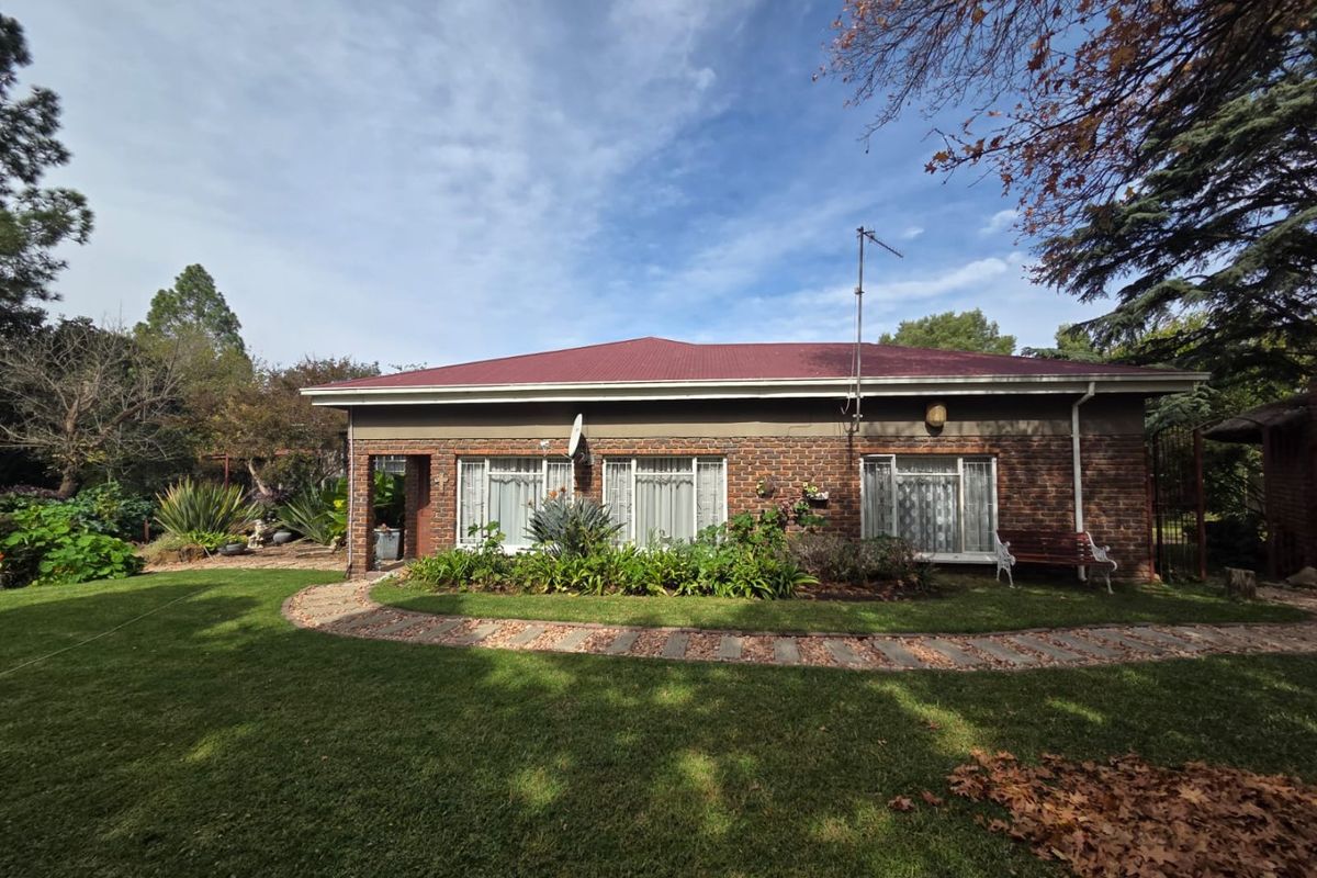 A rear view of a brick house featuring a corrugated metal roof, a paved garden path, and a well-maintained lawn.