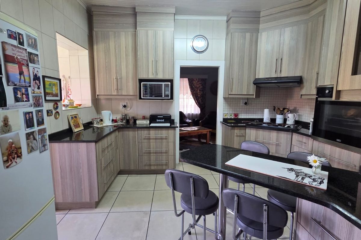A functional kitchen featuring wood-grain cabinetry, granite countertops, built-in oven, hob, and extractor fan with tiled flooring and backsplash.