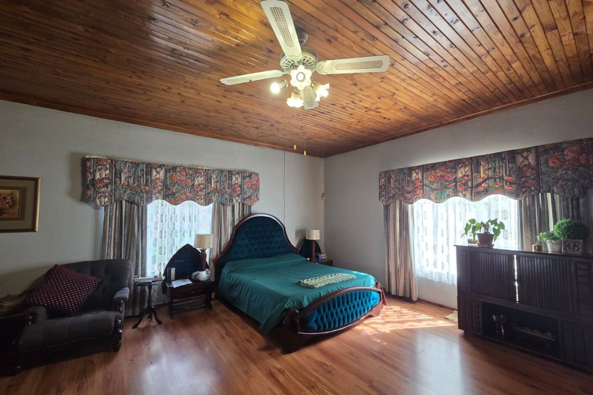 Spacious bedroom featuring a warm timber-paneled ceiling, ceiling fan, and durable laminate flooring, offering a classic and comfortable living space.