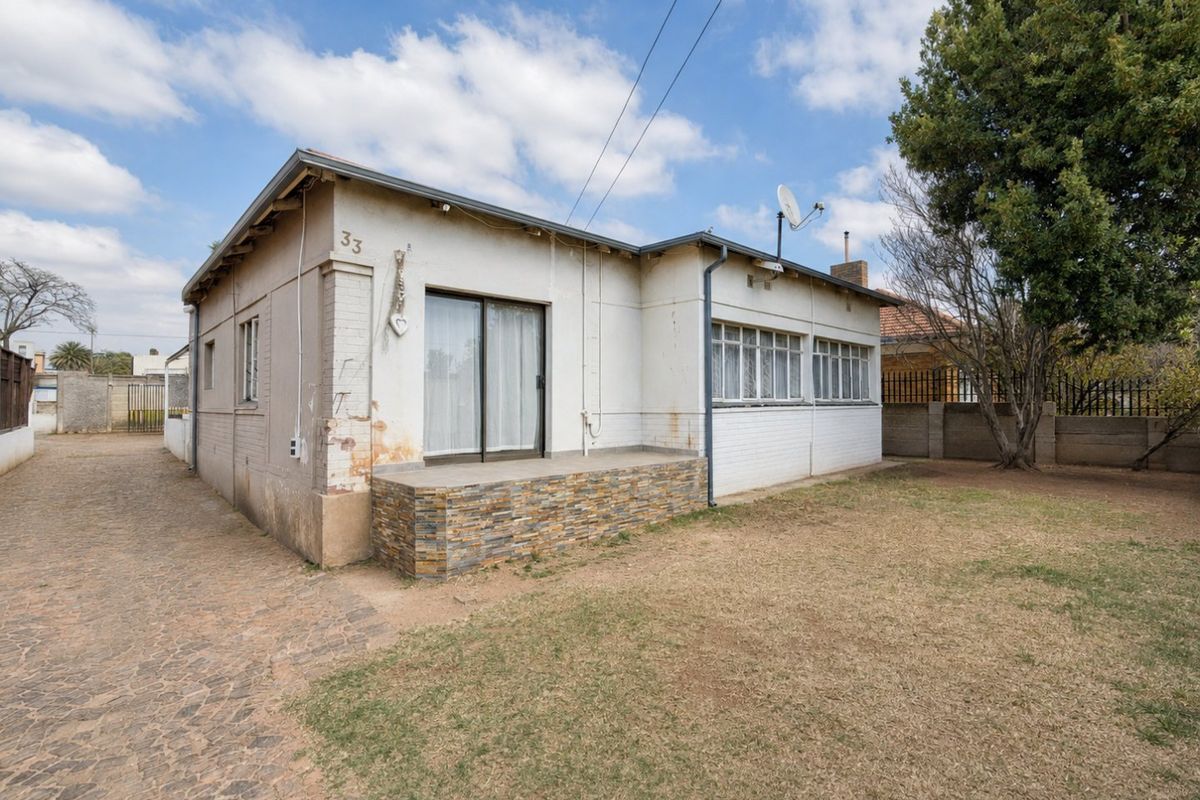 Rear view of a single-story house featuring a paved driveway, a small patio with stone cladding, and a sliding door entrance.