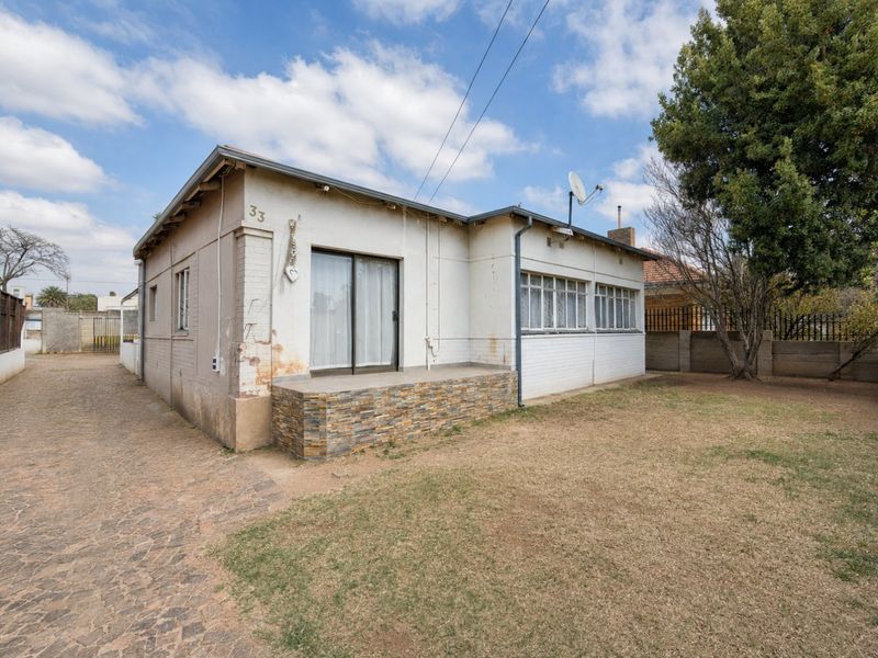 Rear view of a single-story house featuring a paved driveway, a small patio with stone cladding, and a sliding door entrance.