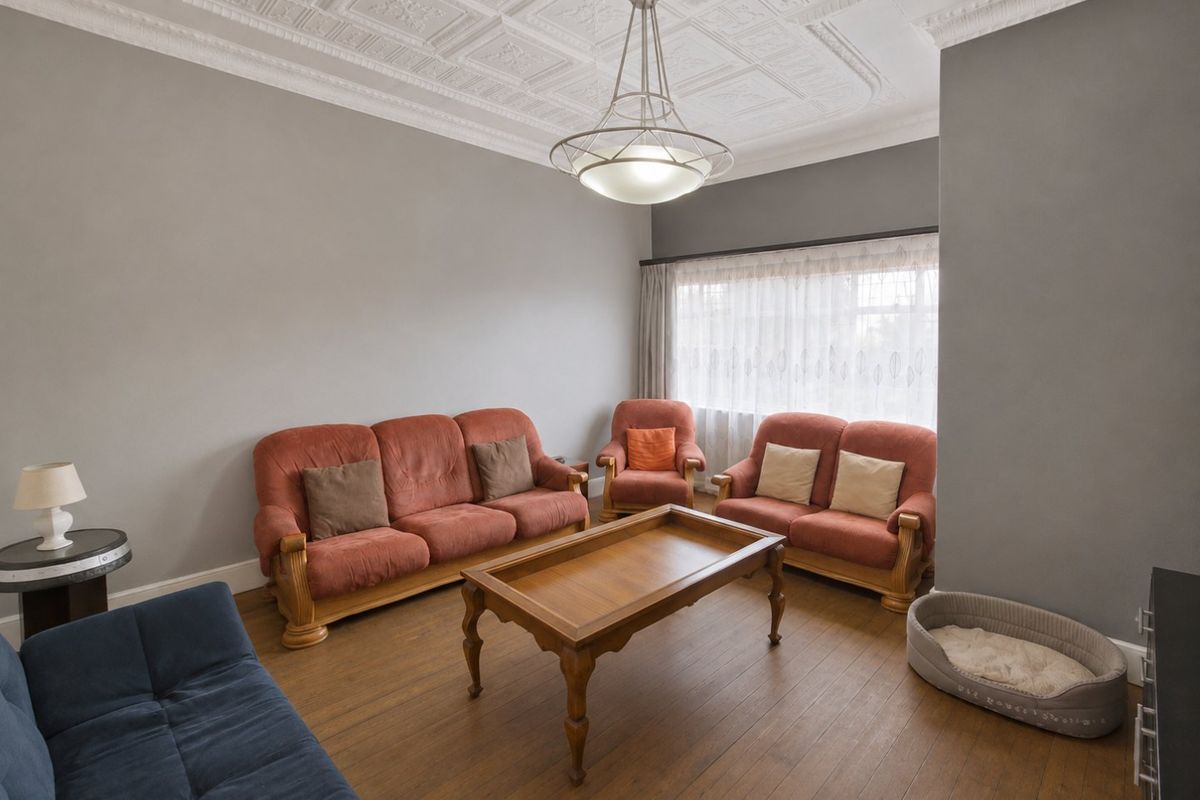 A spacious living room featuring a classic ornate pressed metal ceiling, hardwood flooring, and a central pendant light fixture.