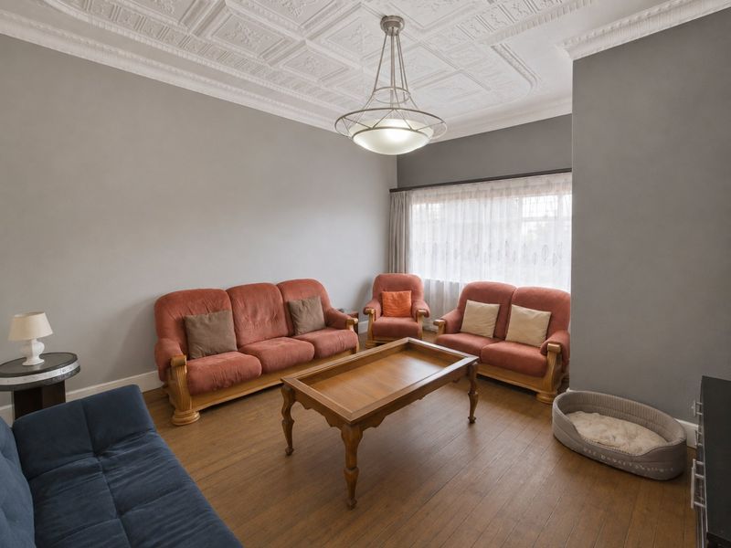 A spacious living room featuring a classic ornate pressed metal ceiling, hardwood flooring, and a central pendant light fixture.