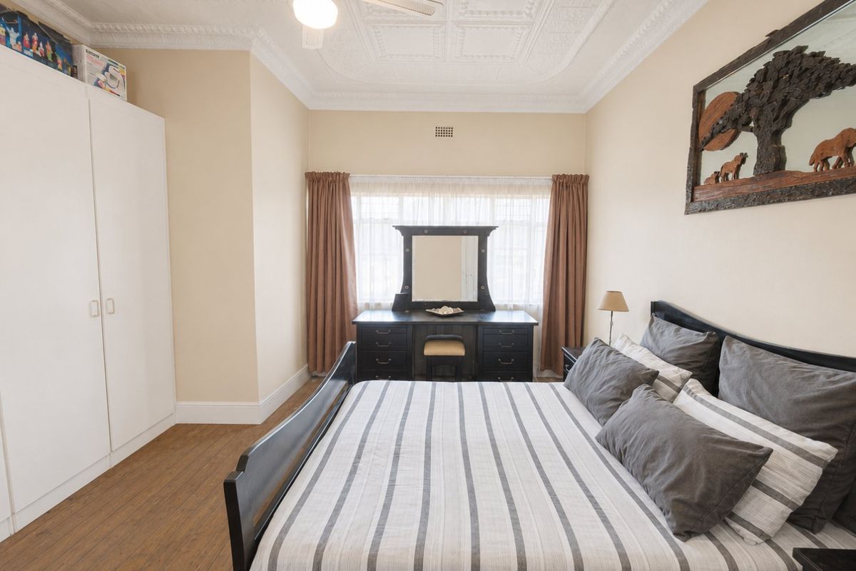 A well-maintained bedroom featuring a decorative pressed metal ceiling, built-in wardrobe, ceiling fan, and laminate flooring.