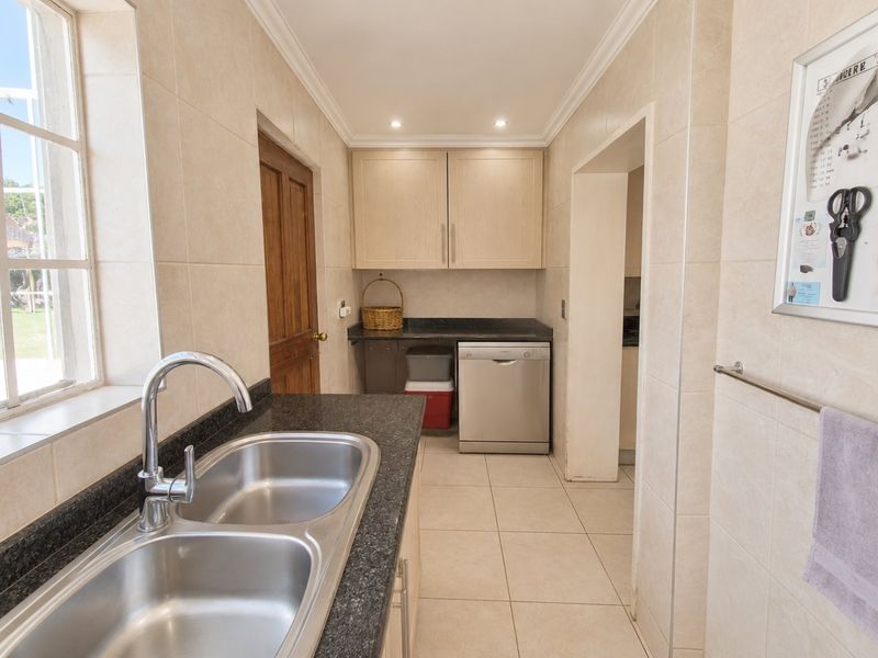 Functional scullery featuring granite countertops, double stainless steel sink, tiled finishes, and ample built-in cabinetry for organized storage.