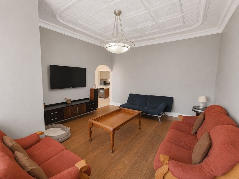 Spacious living room featuring classic coffered ceilings, warm hardwood flooring, and an elegant archway leading to the kitchen area.