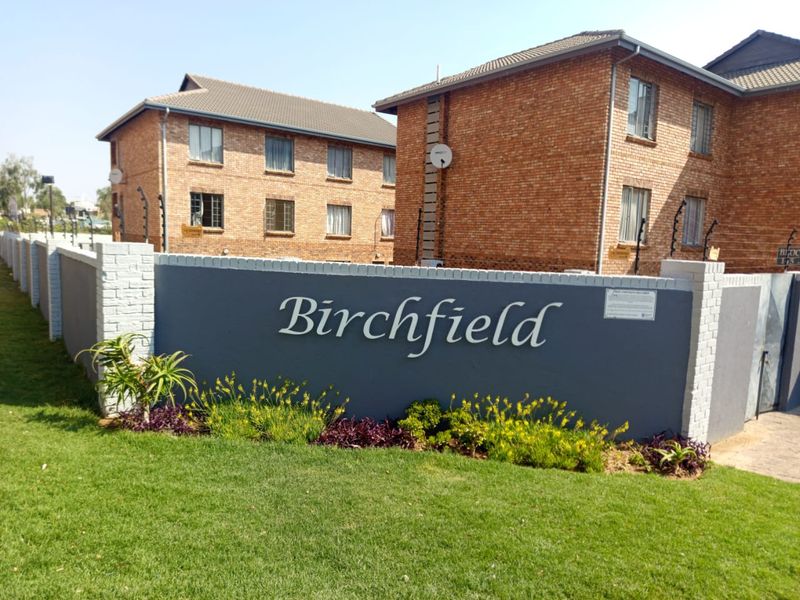 Exterior view of the Birchfield apartment complex featuring face-brick architecture, perimeter walling with electric fencing, and landscaped garden area.