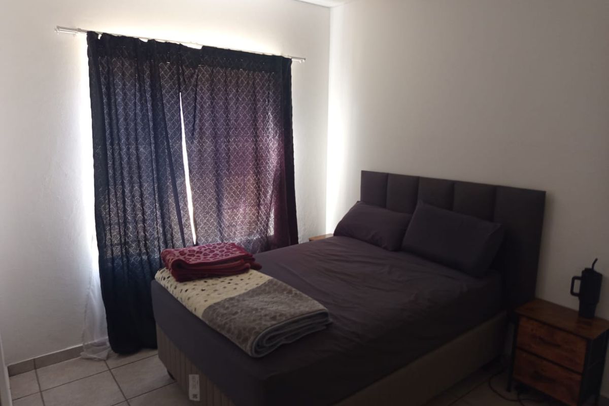 A functional bedroom featuring tiled flooring and a window with a curtain rod, providing a neutral space ready for personalization.