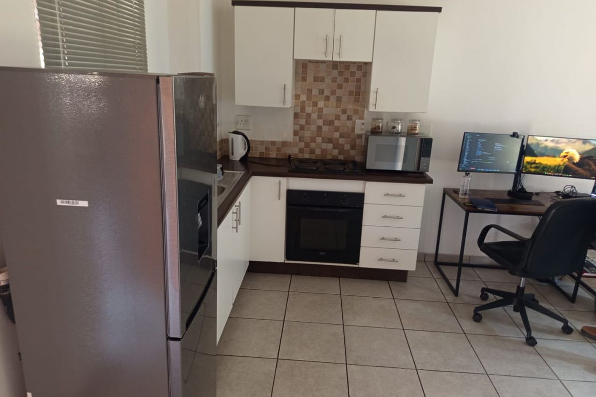 Compact kitchen featuring white cabinetry, mosaic tile backsplash, built-in oven, hob, and ceramic floor tiles, integrated into an open-plan living space.