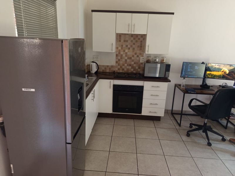 Compact kitchen featuring white cabinetry, mosaic tile backsplash, built-in oven, hob, and ceramic floor tiles, integrated into an open-plan living space.