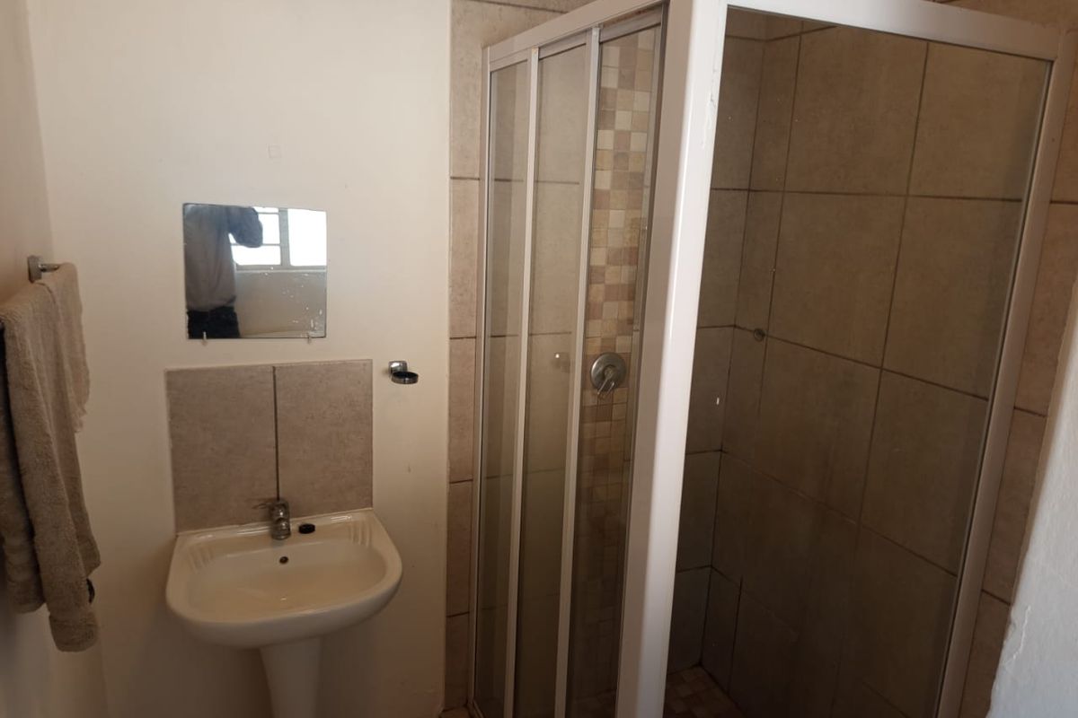 A compact bathroom featuring a pedestal basin and a corner shower enclosure with tiled walls.
