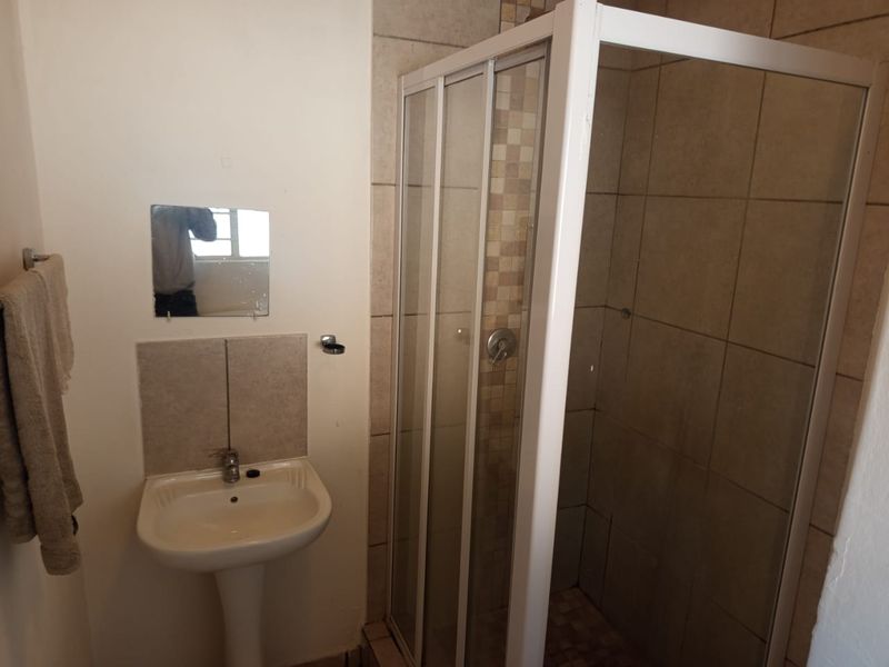 A compact bathroom featuring a pedestal basin and a corner shower enclosure with tiled walls.