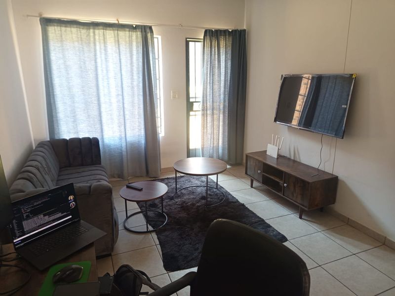 A functional living room featuring tiled flooring, a security gate, and natural light through large windows.