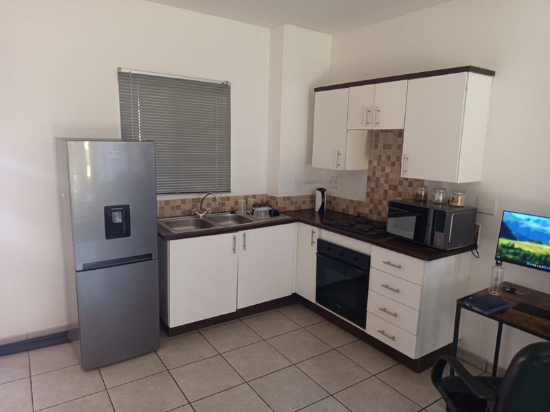 A functional kitchen featuring white cabinetry, dark laminate countertops, a built-in oven, electric hob, and tiled flooring with a neutral backsplash.