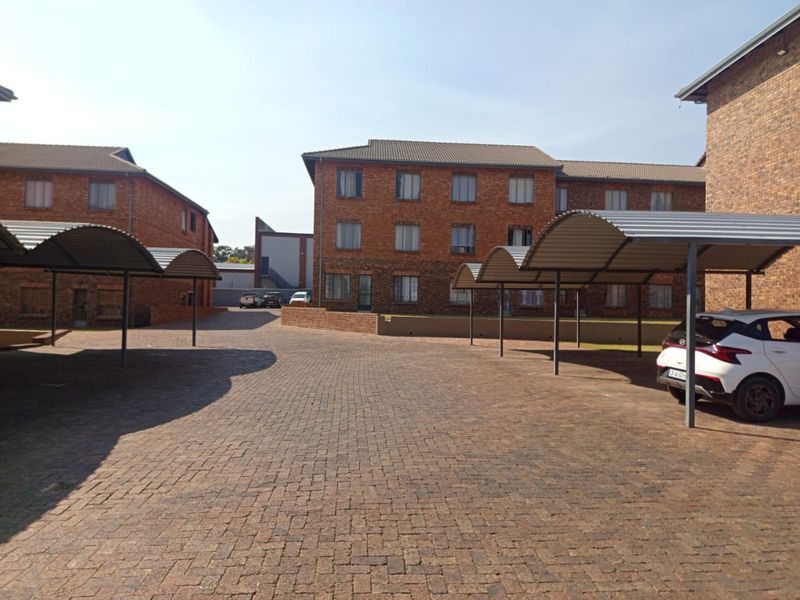 Exterior view of an apartment complex featuring face brick buildings, paved parking area, and covered carport structures.