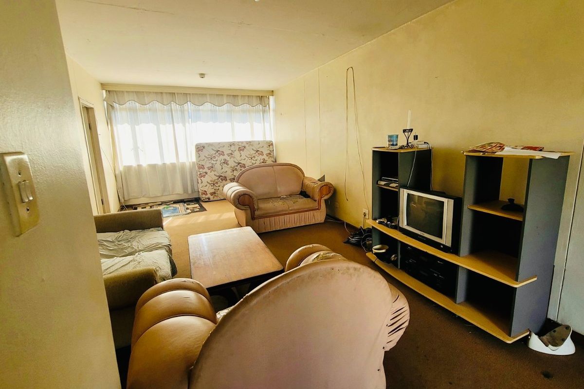 A living room area featuring carpet flooring and large windows with curtain tracks, requiring cosmetic updates and wall refinishing.