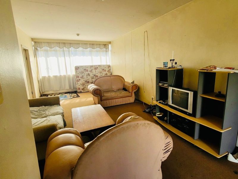 A living room area featuring carpet flooring and large windows with curtain tracks, requiring cosmetic updates and wall refinishing.