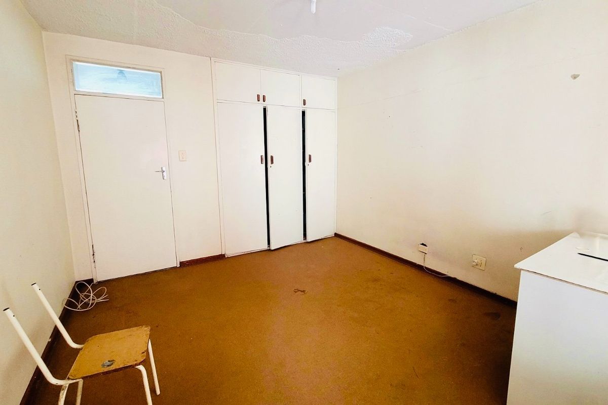 An empty bedroom featuring built-in cupboards, carpeted flooring, and a transom window above the door, offering a blank canvas for renovation.