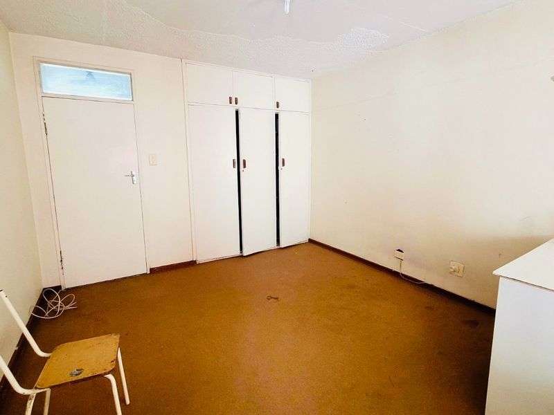 An empty bedroom featuring built-in cupboards, carpeted flooring, and a transom window above the door, offering a blank canvas for renovation.