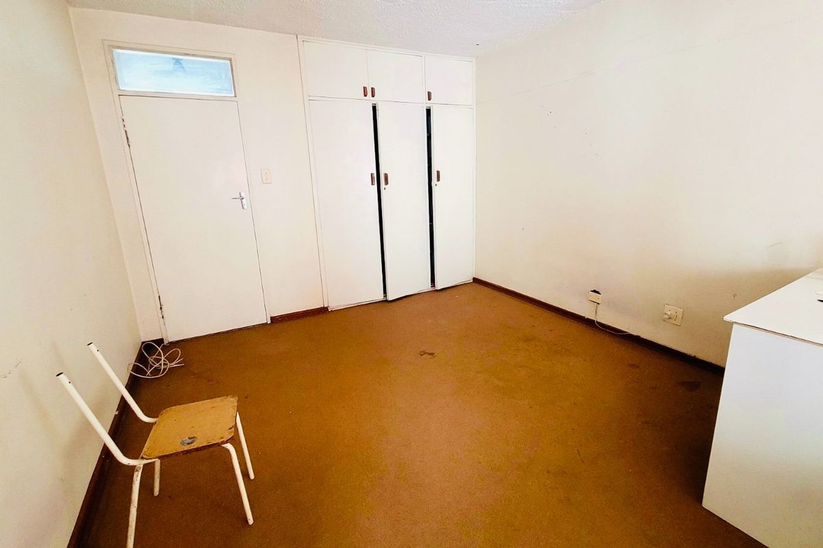 A vacant bedroom featuring built-in cupboards, a standard internal door, and a transom window, requiring cosmetic updates to the flooring and wall finishes.
