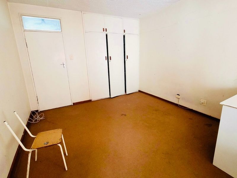 A vacant bedroom featuring built-in cupboards, a standard internal door, and a transom window, requiring cosmetic updates to the flooring and wall finishes.