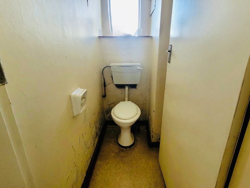 A small, dated bathroom featuring a standard toilet and cistern, currently requiring significant wall repairs and cosmetic updates.