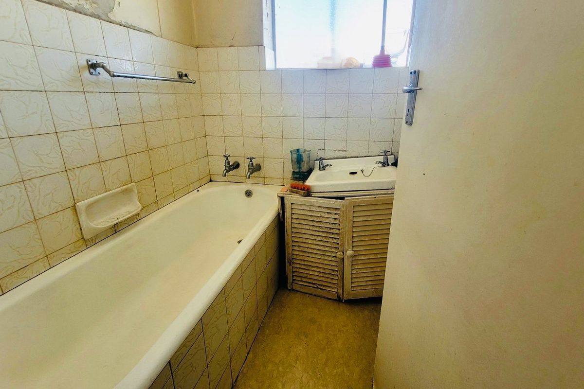 A dated bathroom featuring a standard bathtub, wall-mounted basin with vanity cabinet, and tiled wall finishes in need of renovation.