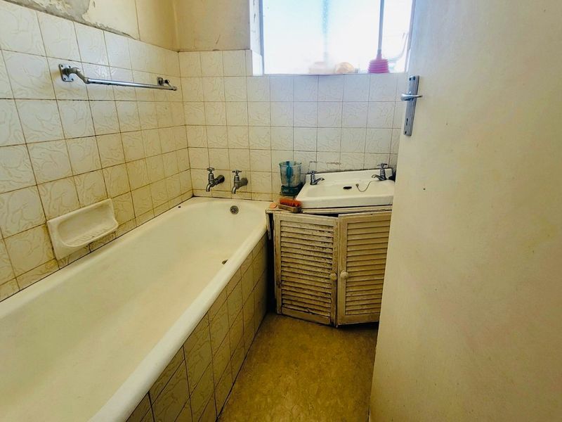 A dated bathroom featuring a standard bathtub, wall-mounted basin with vanity cabinet, and tiled wall finishes in need of renovation.
