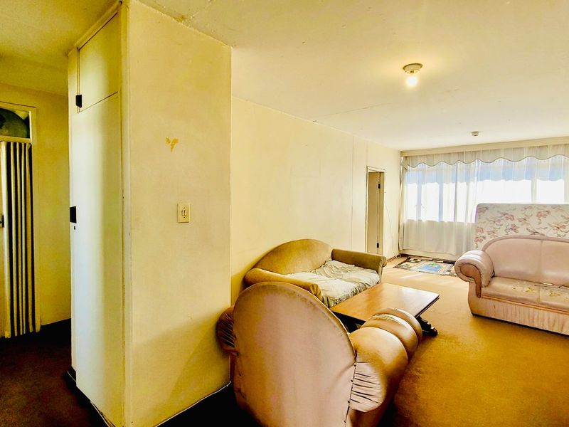 Spacious living area featuring large windows for natural light, carpeted flooring, and a built-in storage cupboard, offering potential for modernization and renovation.