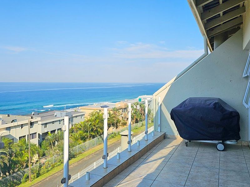 Spacious balcony featuring a glass balustrade and tiled flooring, offering expansive ocean and coastal views.