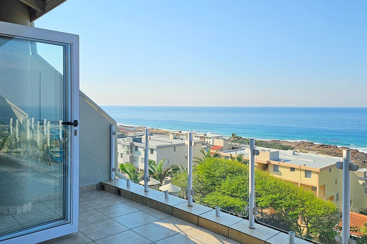 A spacious balcony featuring tiled flooring and a modern glass balustrade, offering expansive, unobstructed views of the coastline and ocean.