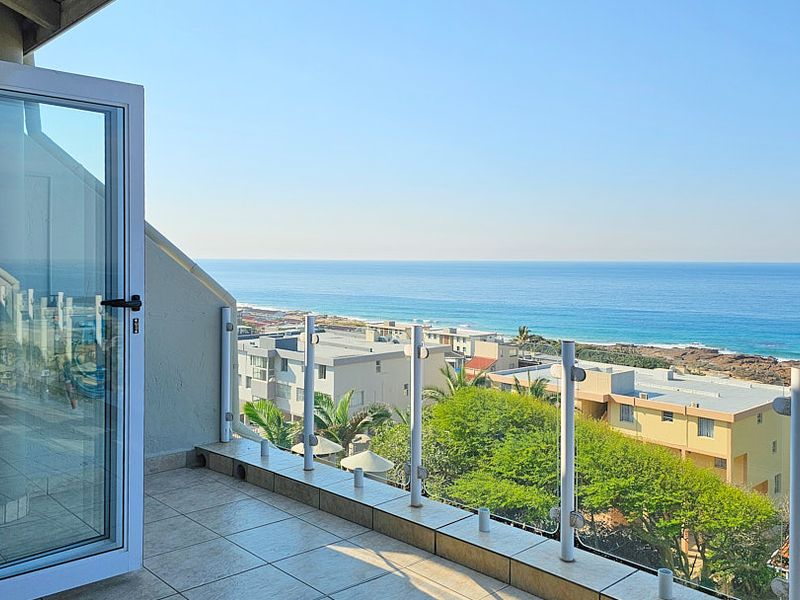 A spacious balcony featuring tiled flooring and a modern glass balustrade, offering expansive, unobstructed views of the coastline and ocean.