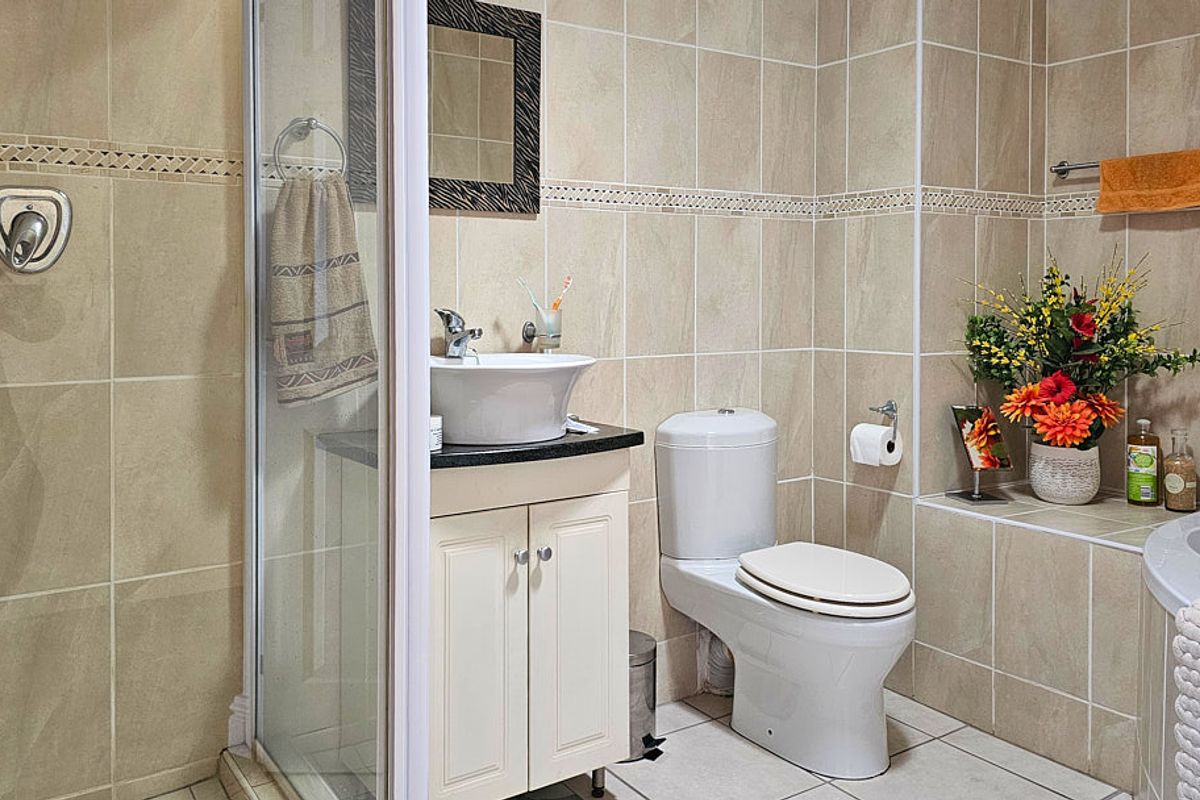 A functional bathroom featuring a shower enclosure, vanity with vessel sink, toilet, and neutral wall and floor tiling.