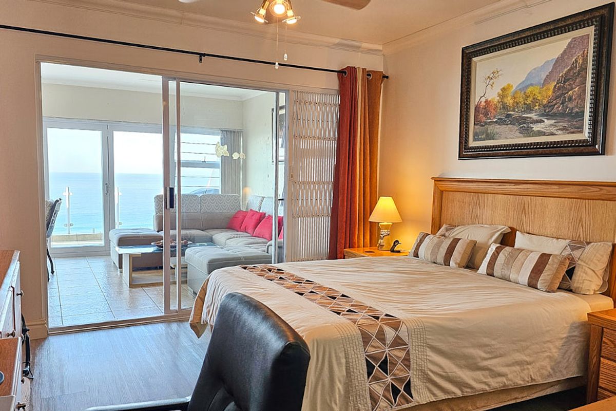 Spacious bedroom featuring laminate flooring, ceiling fan, and large sliding glass doors providing direct access to a balcony with ocean views.